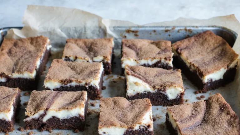 Cream cheese snickerdoodle blondies cut into uneven squares in a baking pan with cinnamon sugar topping
