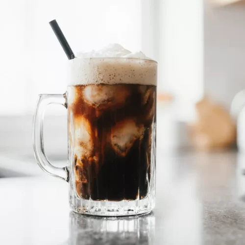 Homemade iced shaken espresso Dunkin style in a clear glass with cold foam in an ordinary kitchen.