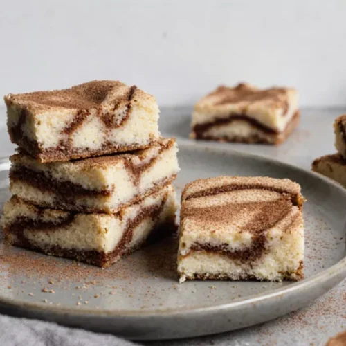 Stack of cream cheese snickerdoodle blondies with cinnamon sugar topping on a plain plate