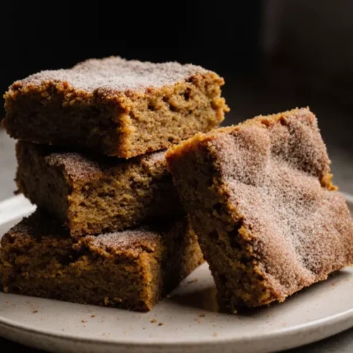 Stack of pumpkin snickerdoodle blondies with cinnamon sugar topping on a plain plate