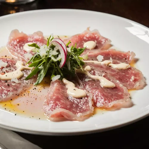 Thinly sliced wagyu carpaccio arranged on a chilled plate with olive oil and salt